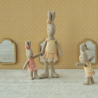 Three stuffed rabbit dolls in ballet attire standing against a patterned wall.