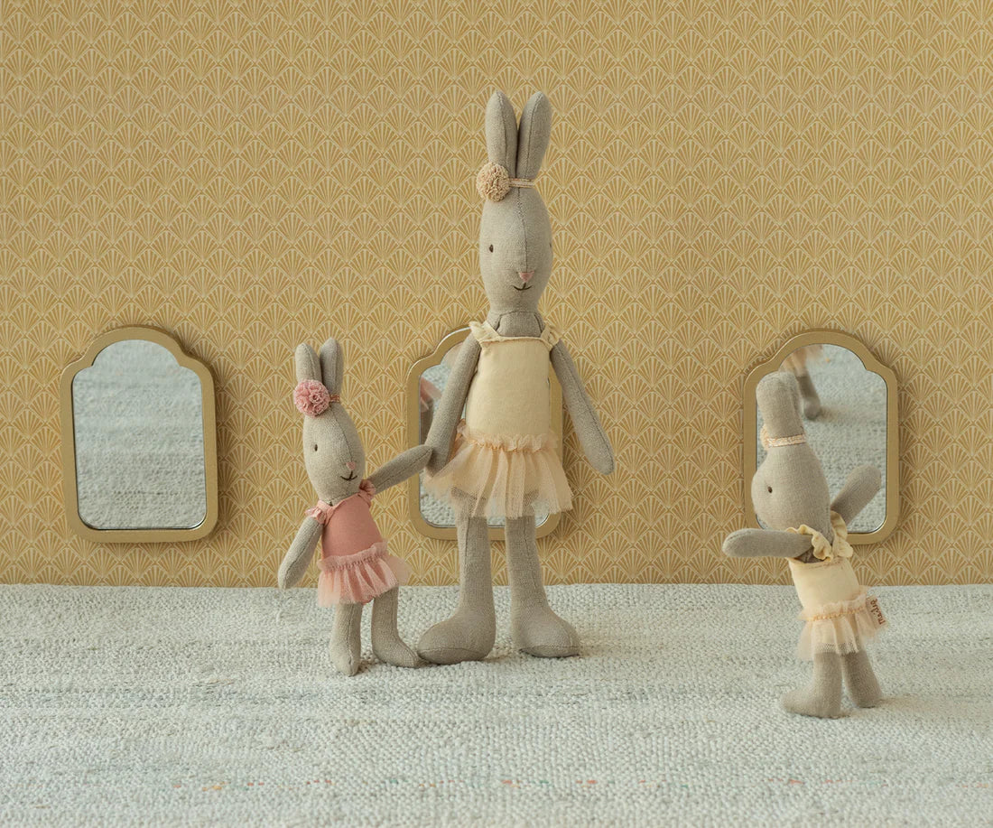 Three stuffed rabbit dolls in ballet attire standing against a patterned wall.
