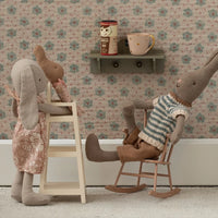 Stuffed rabbit toys in a room with floral wallpaper, chairs and a shelf.
