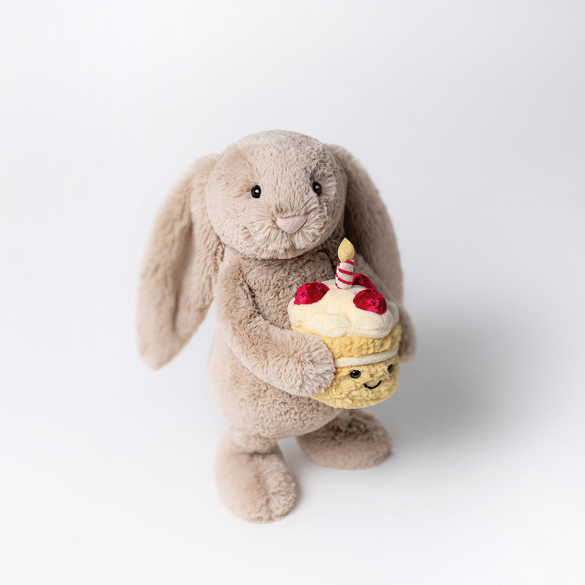 Overhead view of plush  toy rabbit holding a cupcake with a candle on a white background.