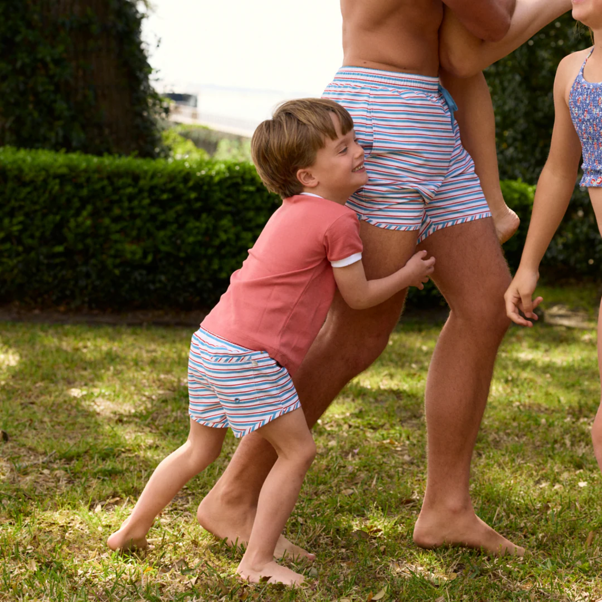 Models wearing red, white and blue  striped boardie swim shorts for him with a blue drawstring 