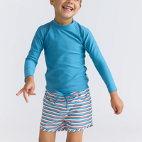 Model wearing red, white and blue  striped boardie swim shorts for him with a blue drawstring and a long-sleeve blue rashguard shirt