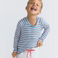 Model wearing striped long-sleeve rashguard top with red, white, and blue colors and white boardie swim shorts with red drawstring