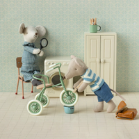 Two toy mice in a room with a tricycle, a washing machine, dresser and chair.