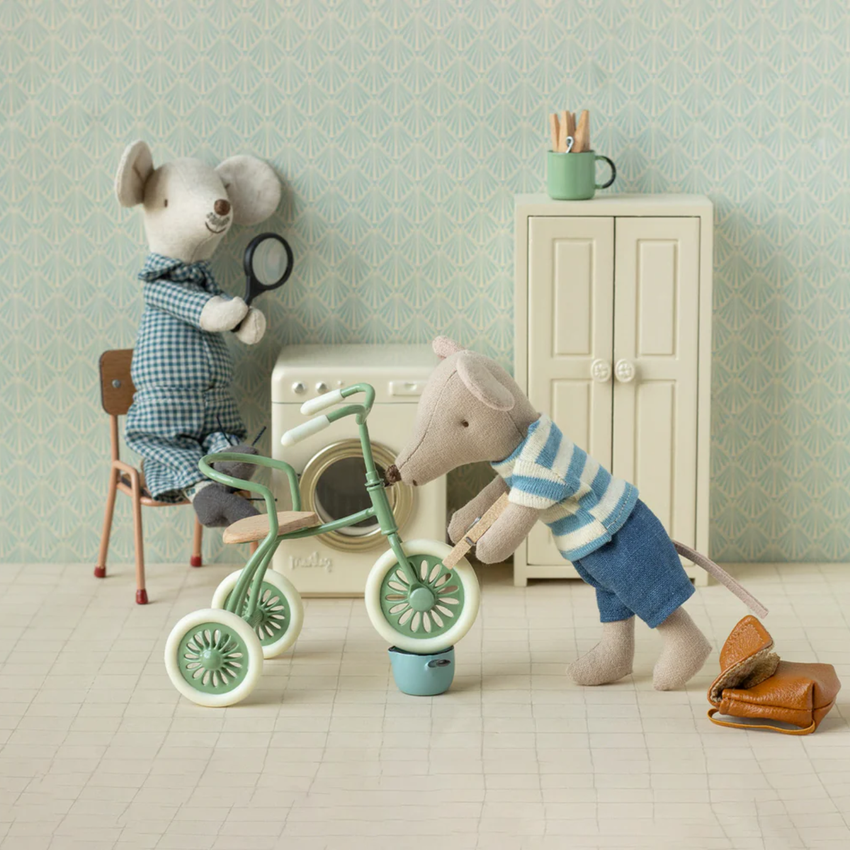 Two toy mice in a room with a tricycle, a washing machine, dresser and chair.