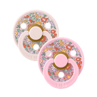 Two pink and white floral-patterned baby pacifiers on a white background.