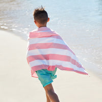 Person wrapped in a pink and white striped towel on a beach.