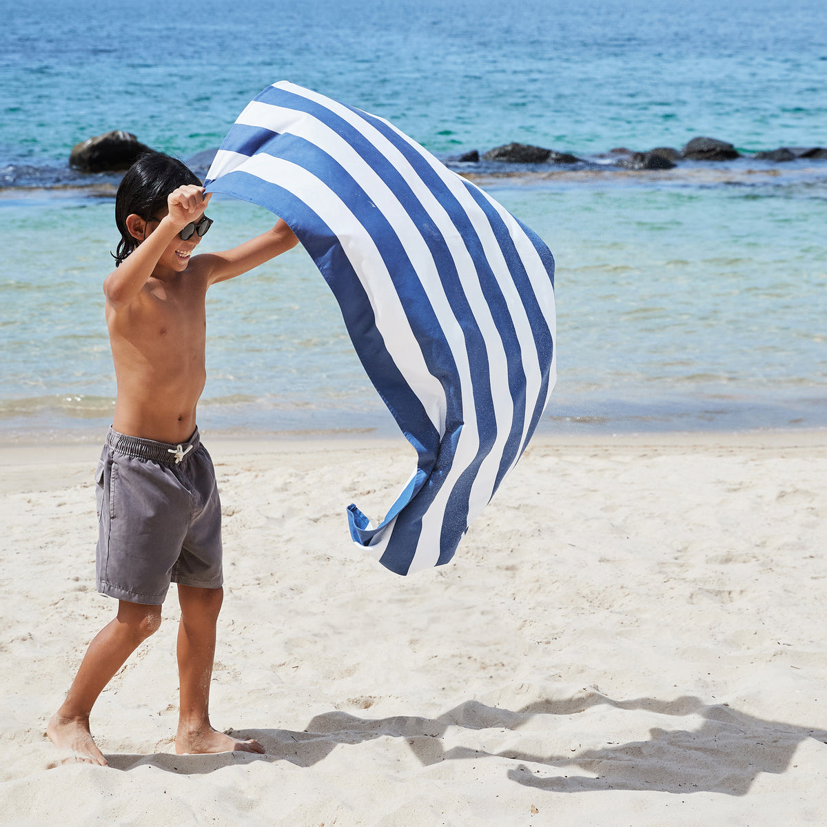 Person on a beach holding a blue and white striped towel.