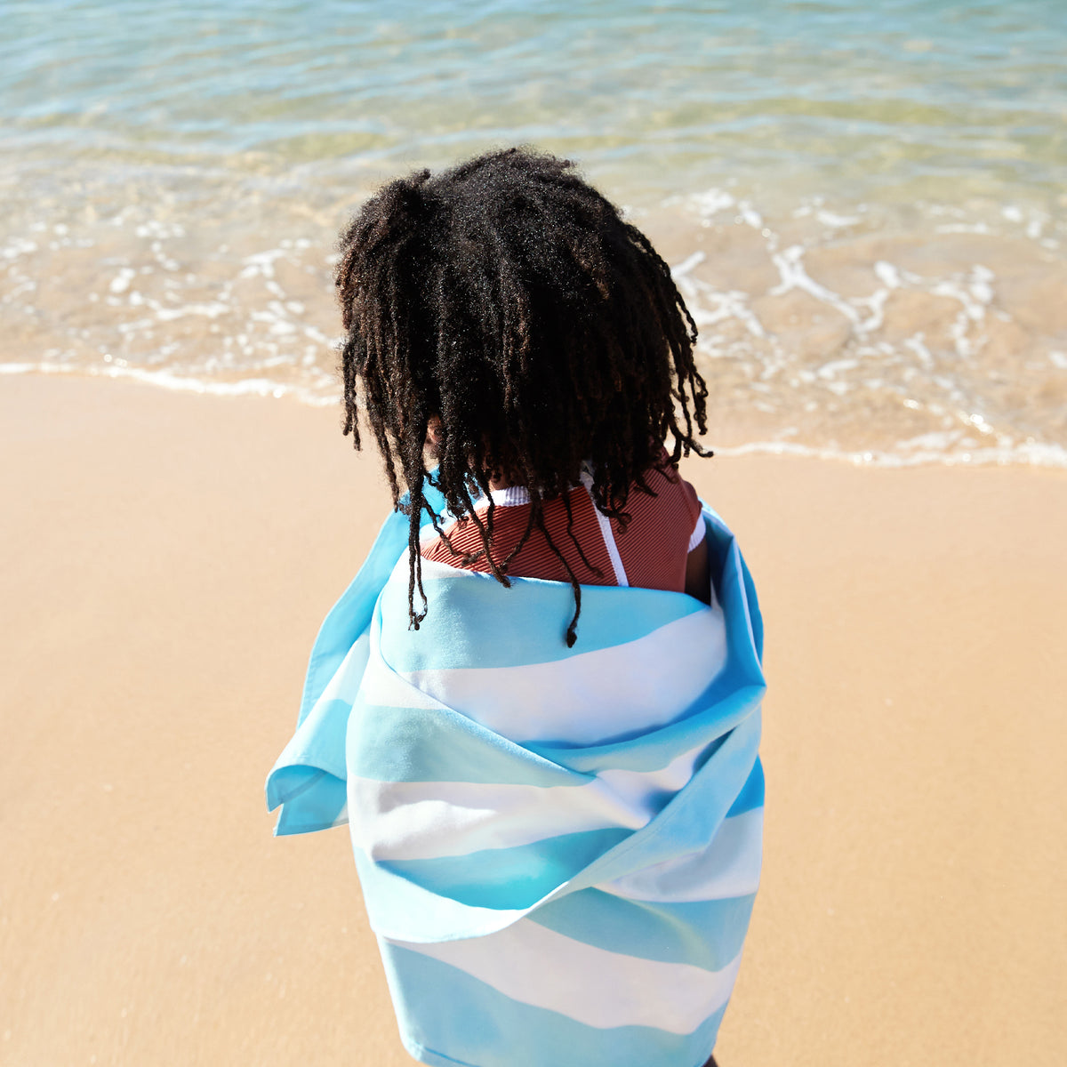 Person wrapped in a blue and white striped towel on a beach.