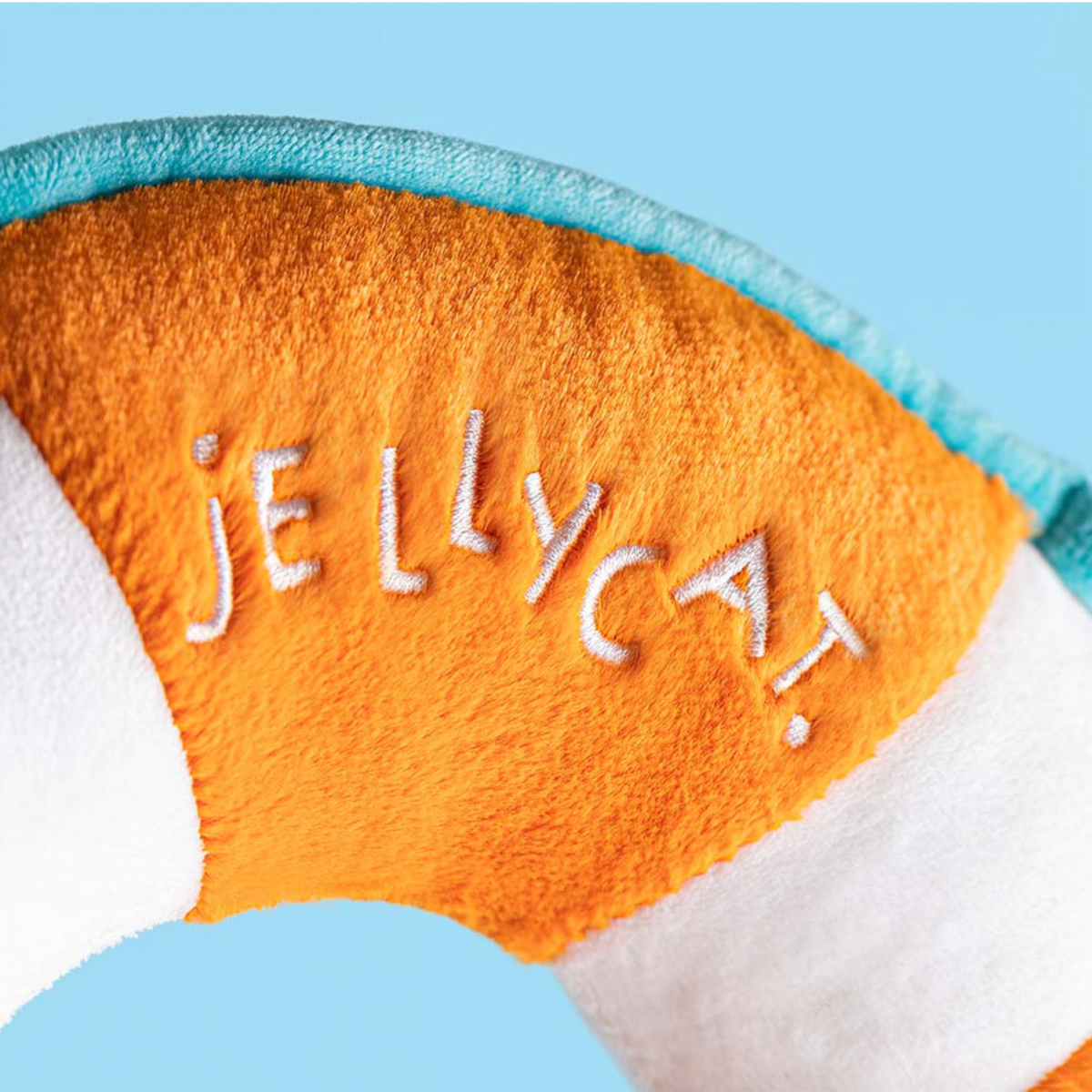 Close-up of a plush toy with 'Jellycat' branding on an orange and white background.