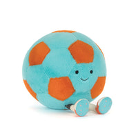 A plush soccer ball toy with a light blue body, orange panels, and a smiling face, sitting on a white background.