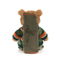 A teddy bear viewed from behind, wearing an olive green sleeping bag and dark striped knit sweater, photographed on a white background.