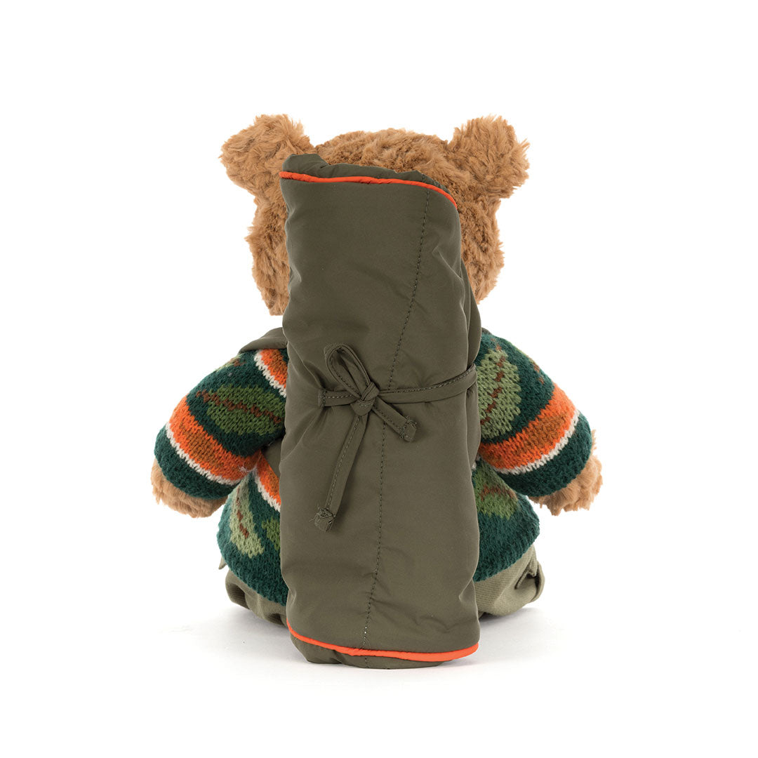A teddy bear viewed from behind, wearing an olive green sleeping bag and dark striped knit sweater, photographed on a white background.