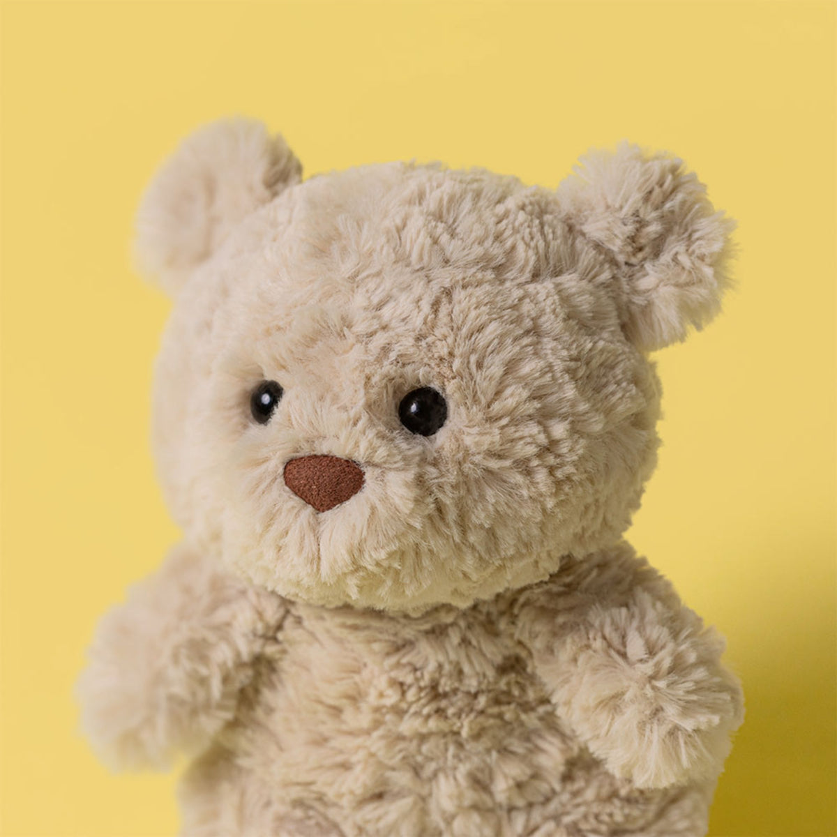 Close up image of a cream stuffed bear plush on a yellow background.
