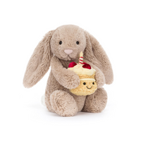 Beige plush toy rabbit holding a cupcake with a small face on a white background.