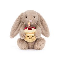 Plush beige bunny holding a cupcake with a candle on a white background.
