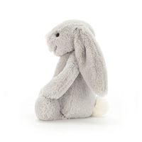 Side view of a  light gray silver plush bunny toy sitting on a seamless white background.