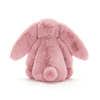 A pink plush bunny toy shown from the back, featuring long floppy ears, a soft furry body, and a small pom-pom tail, photographed on a clean white background.
