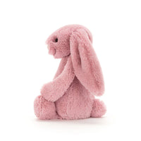 Side view of a pink plush bunny toy with long floppy ears, sitting in profile against a clean white background.