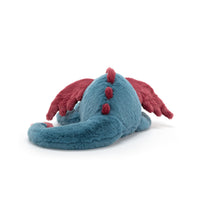 Back view of a plush dragon toy in teal blue with dark red wings and red back spikes, photographed on a clean white background.