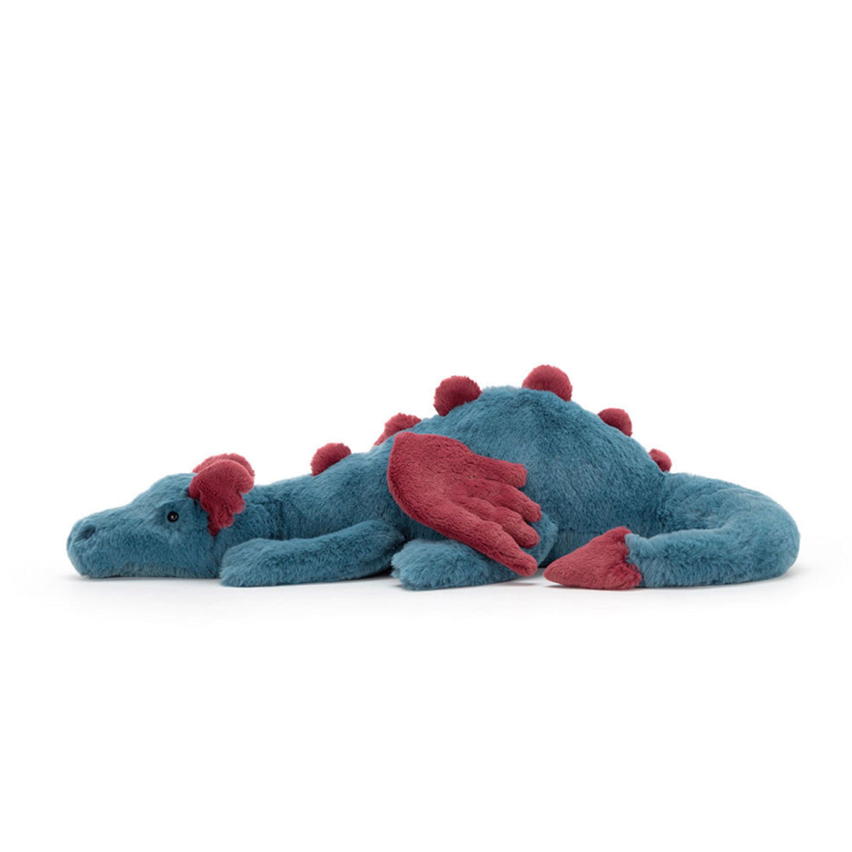 Side view of a plush toy dinosaur with a blue body and red spikes, wings, and head details, lying down on a white background.