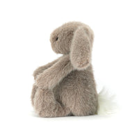 A plush stuffed bunny toy in a soft taupe-gray color, sitting with its arms crossed over its knees on a clean white background.