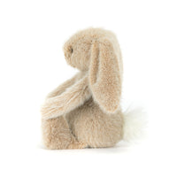 Side view of a  plush stuffed bunny toy in a light beige/tan color, sitting on a seamless white background.
