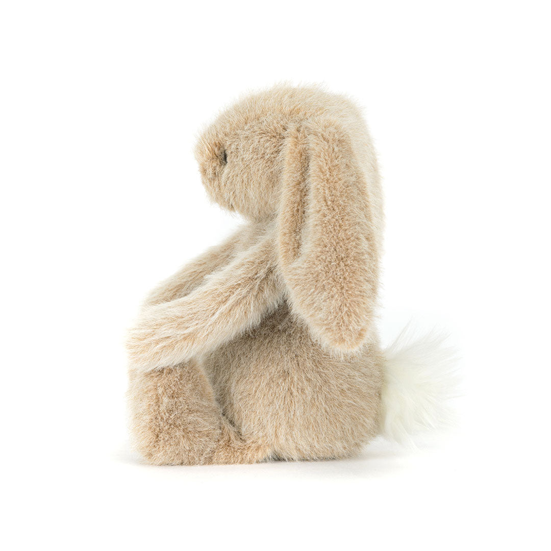 Side view of a  plush stuffed bunny toy in a light beige/tan color, sitting on a seamless white background.
