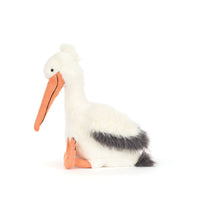 A plush stuffed pelican toy sitting on a plain white background. The toy has white fur, a long orange beak, orange legs, and a dark gray back and tail.