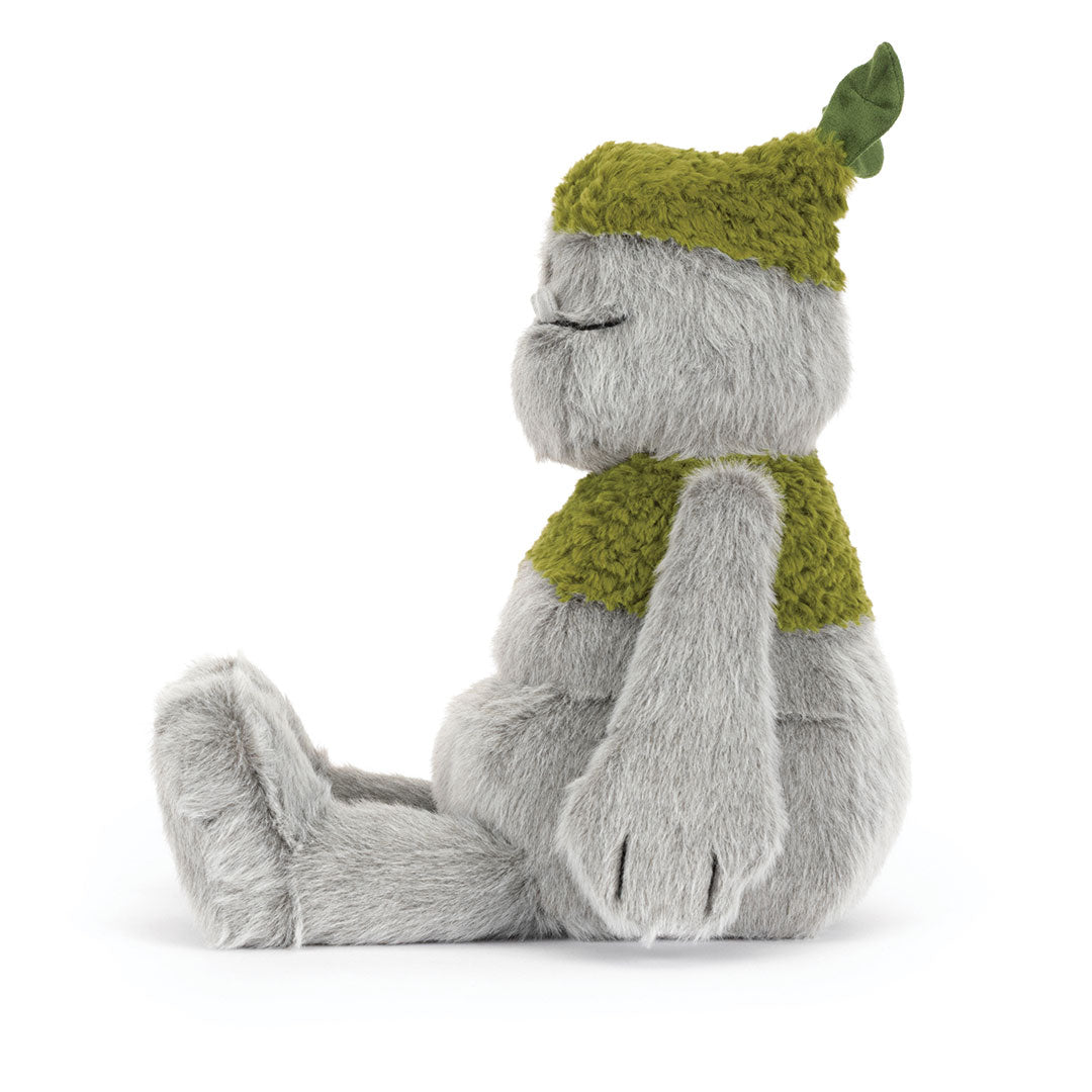 A plush toy figure with soft gray fur sitting in profile, wearing a textured olive-green knit hat with a leaf detail and a matching green knit scarf, photographed on a white background.