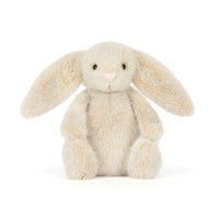 A plush stuffed bunny toy in a soft cream-beige color with long floppy ears, small black eyes, and a tiny pink nose, photographed on a clean white background.