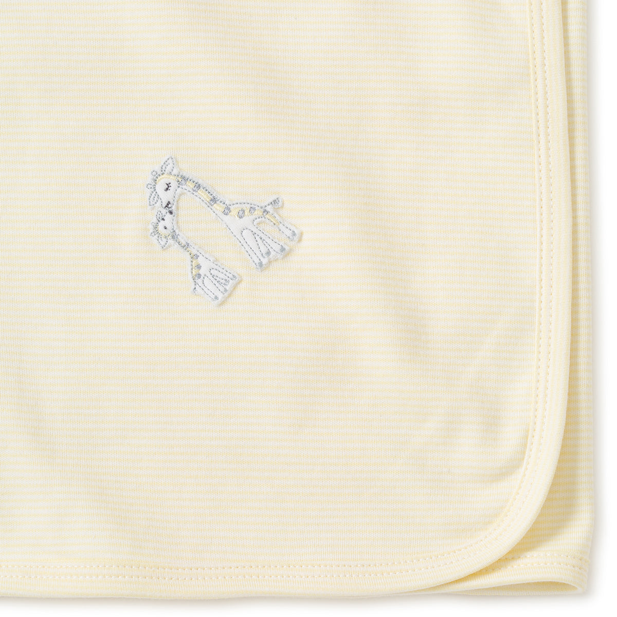 Close-up of a folded yellow receiving  blanket with giraffes embroidery on a white background.