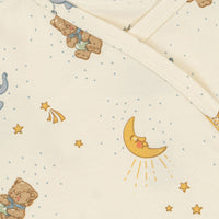 Close-up of a baby body suit in warm off-white, printed with a cute night sky pattern featuring teddy bears, a yellow crescent moon, stars, and small blue dots.