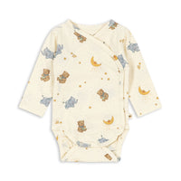 A long-sleeve cross body baby wrap bodysuit in cream with a print of teddy bears, elephants, crescent moons, and stars, shown flat on a white background.