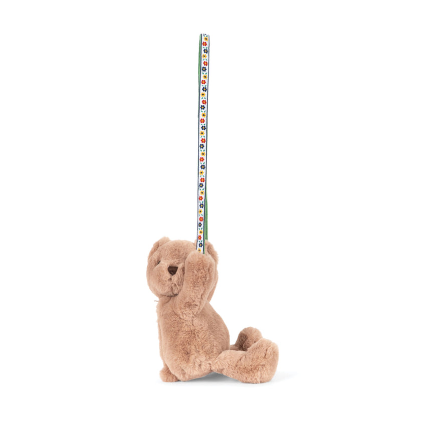 Side view of small bear holding a ribbon in front paws shown on a white background.