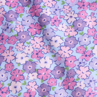 A close-up of a light blue fabric with a dense floral pattern featuring pink, purple, and white flowers with small green leaves.