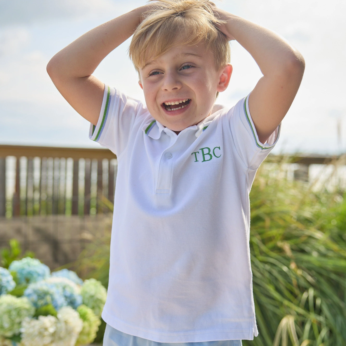 Young boy wearing a white polo shirt with 'TBC' embroidery outdoors.