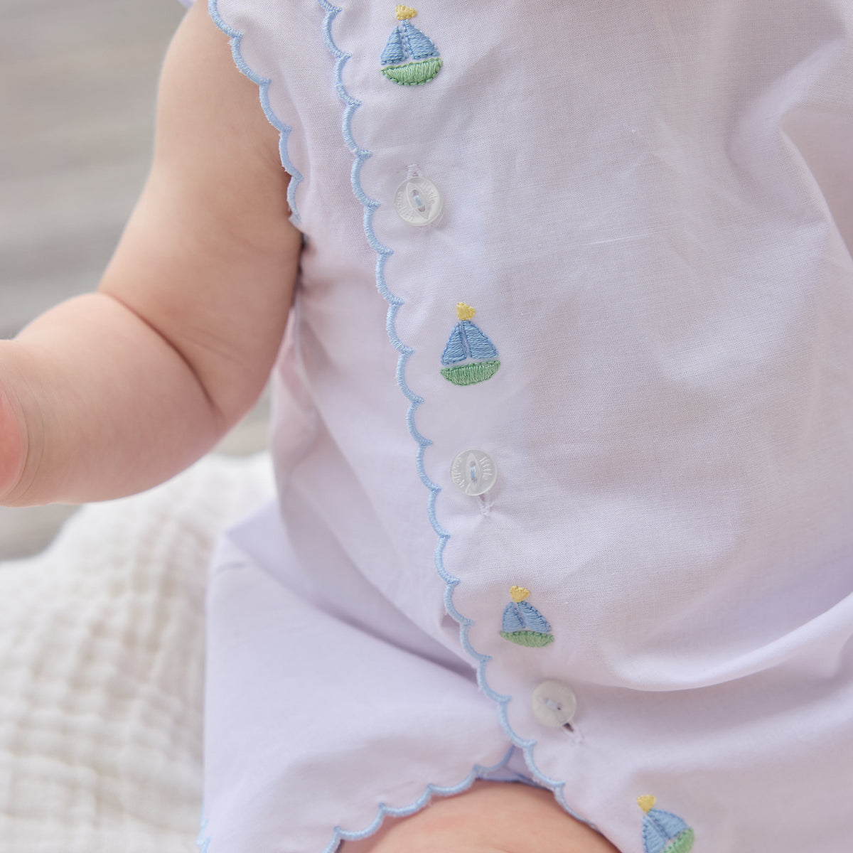 Close-up of a baby's outfit with embroidered sailboats on a neutral background.