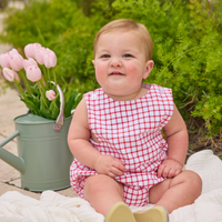Baby wearing red and white window pane romper on a blanket in the backyard.