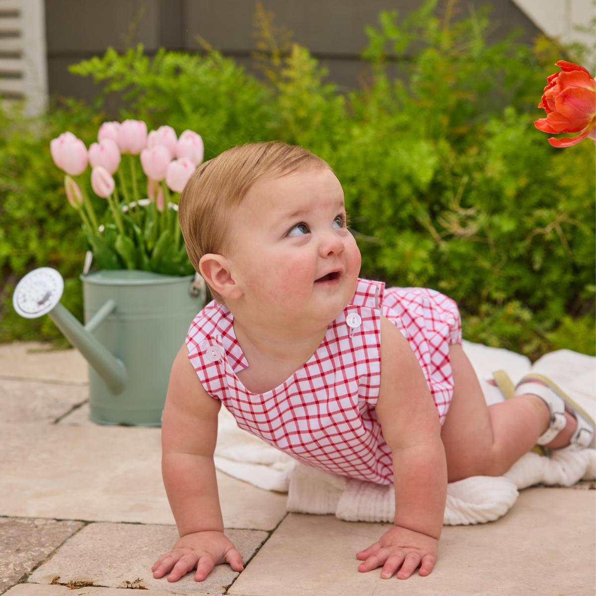 Baby wearing red and white window pane romper in a backyard.
