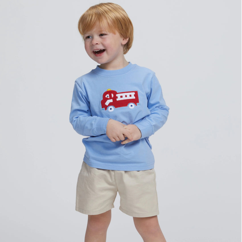 Child wearing long sleeve blue shirt with fire truck applique and khaki pull on shorts shown on a white background.