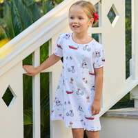 Young girl wearing a white dress with outdoor activity print - biking, boating, puppies - standing on a staircase.