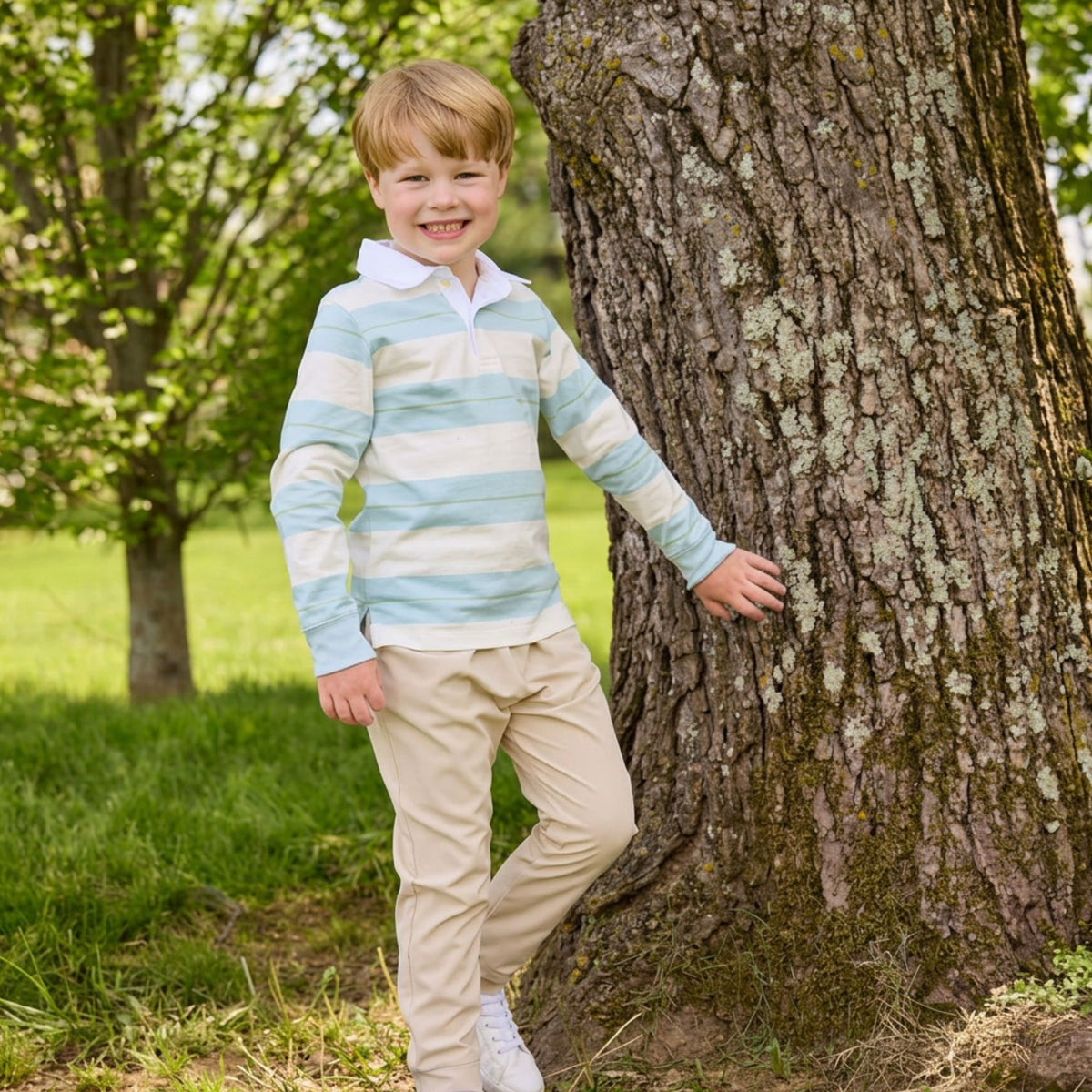 Boy standing near a tree wearing a rugby style shirt and khaki pants.