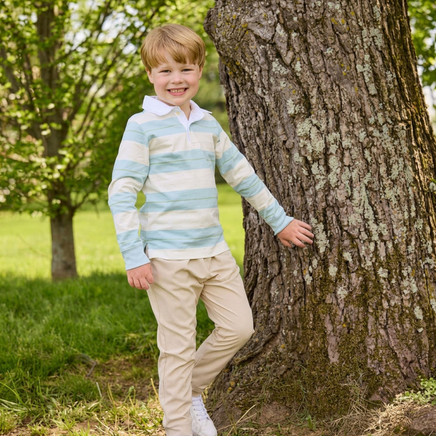 Boy standing near a tree wearing a rugby style shirt and khaki pants.