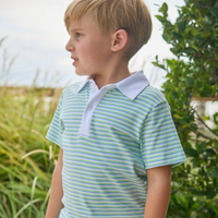 Young boy wearing a striped green and white polo shirt outdoors with greenery in the background.
