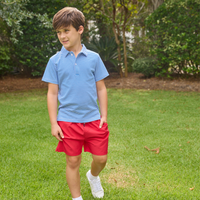 Young boy wearing a blue and white striped polo shirt and red shorts standing on grass.