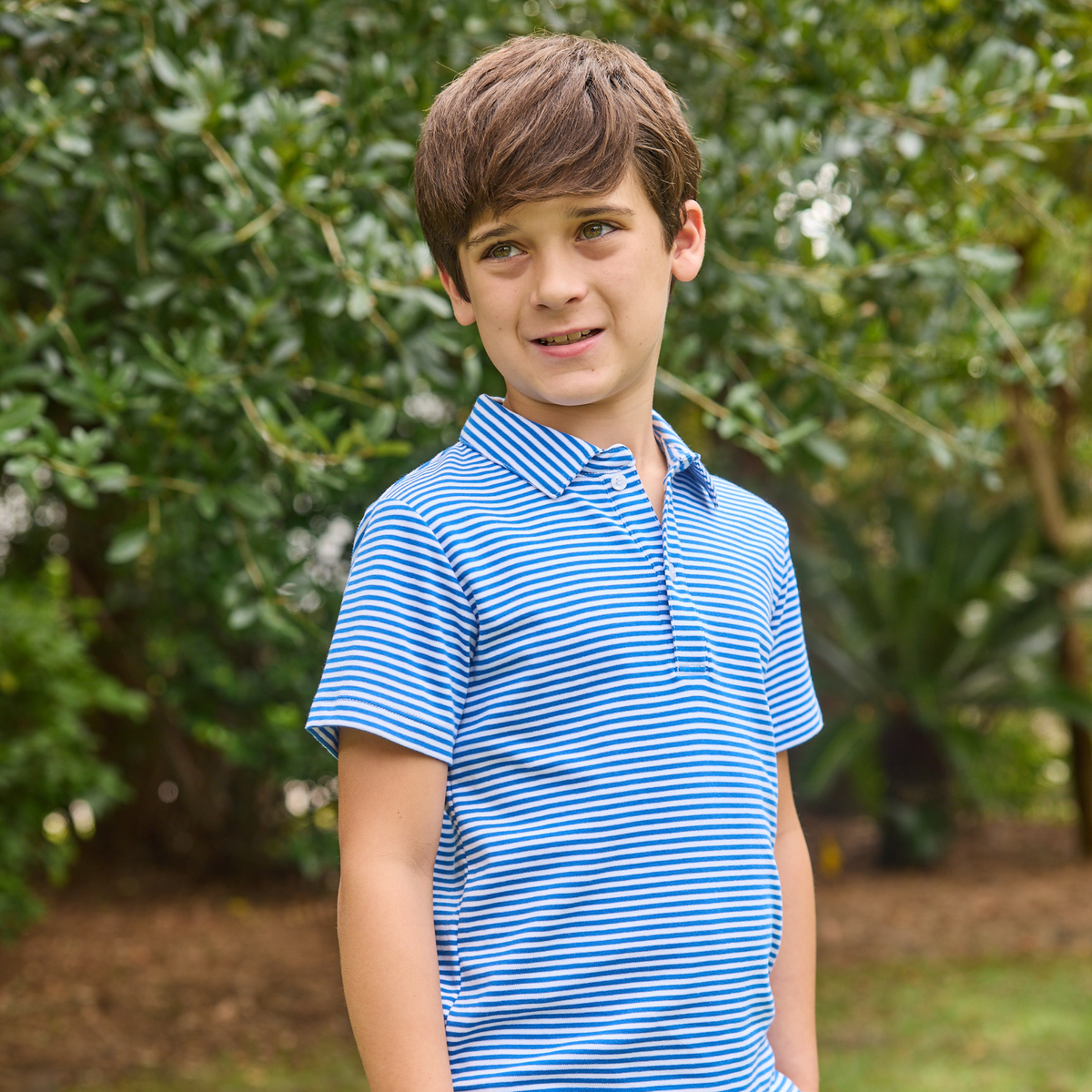 Boy wearing blue and white striped polo shirt in a backyard setting.