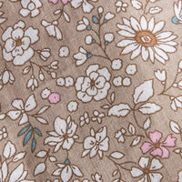 A close-up of a woven fabric with a floral pattern on a warm taupe background. The design features white daisies and other flowers with brown outlines, small pink blossoms, and tiny blue accents.