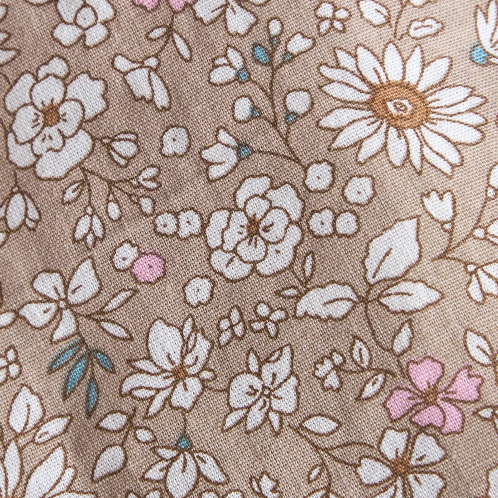 A close-up of a woven fabric with a floral pattern on a warm taupe background. The design features white daisies and other flowers with brown outlines, small pink blossoms, and tiny blue accents.