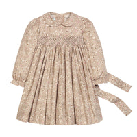 A long-sleeve children's dress in a beige and brown floral print, featuring a smocked bodice, Peter Pan collar, and a tie belt on the side, shown against a plain white background.